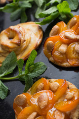 Tart with apricot and apple. Traditional french pie with fruits on dark marble background. Decorated almonds and mint leafs. Delicious dessert with copy space closeup.