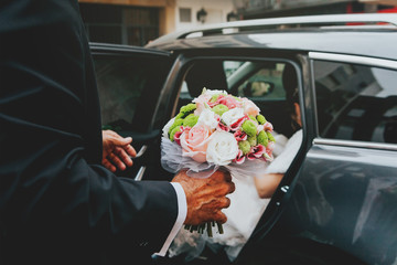 Godfather holding a wedding bouquet and opening the car door to the bride.