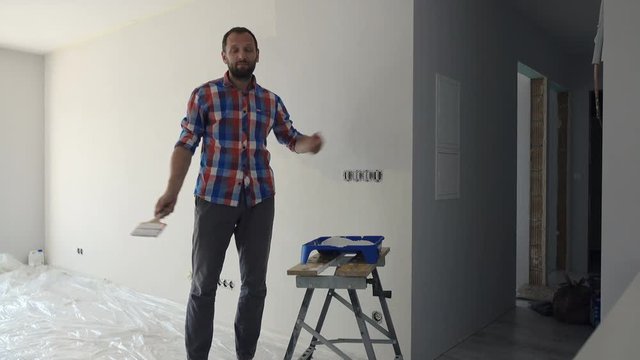 Unhappy man talking to camera while painting wall at his new home
