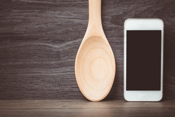 Smartphone and wood spoon on wooden table. Concept online food, Eating technology. Toned photo.