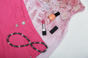 Girl accessories lipstick, nail polish and necklace on pink clothes