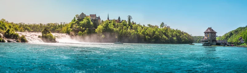 Papier Peint photo Lavable Panoramique La chute du Rhin par une journée ensoleillée - Panorama avec la Rhienfall, le château de Laufen et le château de Worth, tandis que des bateaux naviguent sur les eaux bleues du fleuve, en Suisse.