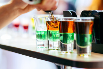 Bartender pouring alcoholic cocktail in shot glasses on bar