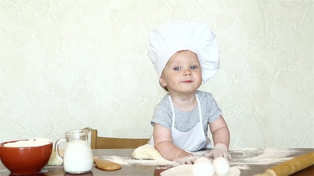 The little boy in a suit of the cook sculpts dough. Baby make dinner in chef suit