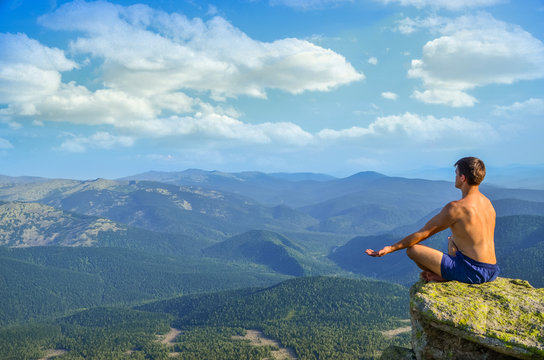 on top of a high mountain cliff in front of a man sitting in the lotus position and meditates. a man sitting on top of a mountain in the lotus position.