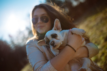Young girl playing with a French bulldog puppy in a park.