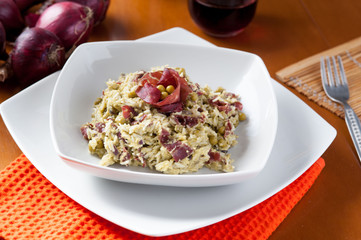 Risotto con bresaola e piselli nel piatto di ceramica bianca sulla tavola apparecchiata