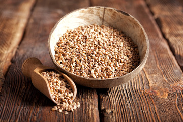 Buckwheat in scoop and bowl on wooden table