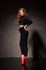 Red-haired woman posing against of black wall in light