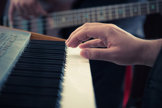 Hand playing music keyboard and bass guitar player in the background. Detail form a concert.     