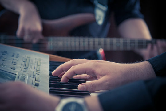 Hand playing music keyboard and bass guitar player in the background. Detail form a concert.     