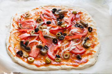 Raw homemade pizza with tomatoes, olives, sweet pepper