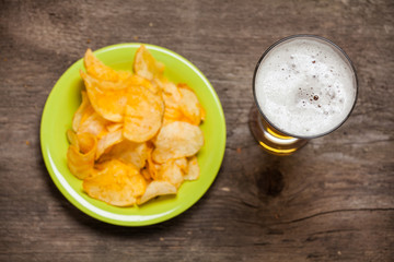 Glass of beer with chips on a wooden background. Top view.