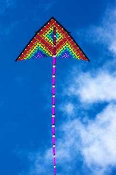 Rainbow colored kite flying high against sunny blue skies for Summer and vacation concept.
