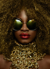 Close-up portrait of magic golden african american female model in massive sunglasses with bright...