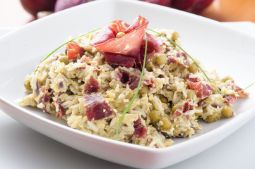 Risotto con bresaola e piselli nel piatto di ceramica bianca sulla tavola apparecchiata
