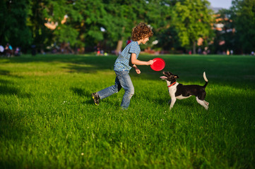 Blonde boy playing with his black and white dog on the lawn in the park.