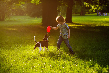 The boy of 8-9 years trains in park with the dog.