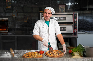 Chef cuts freshly prepared pizza on a wooden substrate.