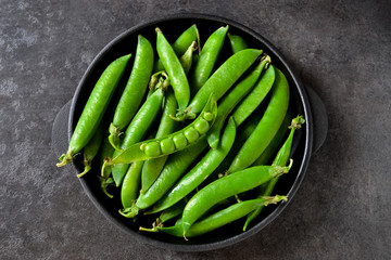 Green, young peas in a cast-iron plate on a black background