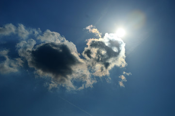 Fototapeta premium Słońce wychodzące zza ciemnej chmury na błękitnym niebie