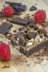 Piece of brownie with chocolate and several strawberries on the light wooden background