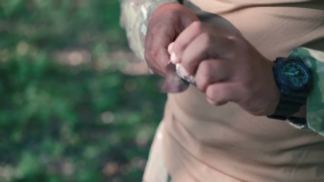 Close up of soldier sharpen knife with bilestone in the forest. Slow motion