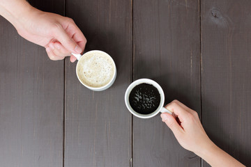joint coffee break with a different taste/ Two hands holding a cup of coffee with a variety of different sorts, against a wooden table top view 