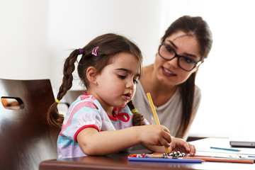 Mother learning her daughter to draw with colorful pencils.