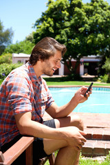 Young man sitting by pool holding cellphone