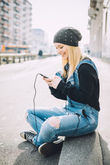 Young beautiful blonde straight hair woman sitting on the ground using smart phone hand hold looking down the screen  smiling - happiness, technology, social network concept