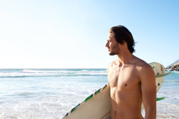 Handsome man holding surfboard at beach