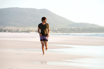 Young man running barefoot on beach
