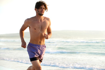 Fototapeta na wymiar Handsome young man running shirtless on beach