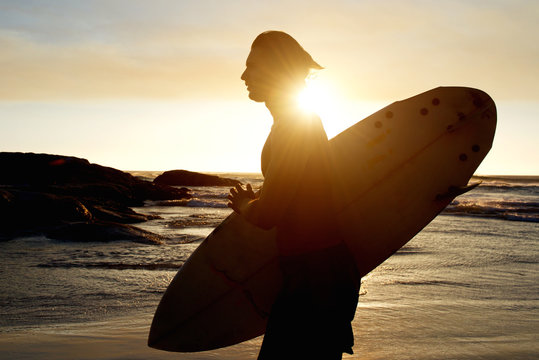 Young man carrying a surfboard at sunset
