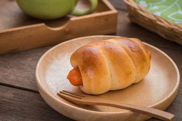 Bread roll with sausage on wooden plate and coffee cup
