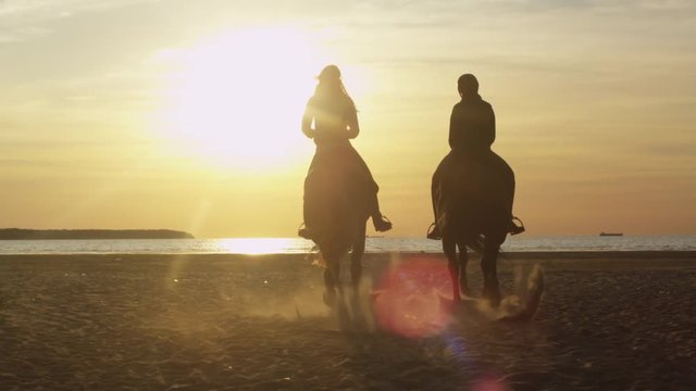 Silhouette of Two Young Women Riding Horses on Beach. Shot on RED Cinema Camera.