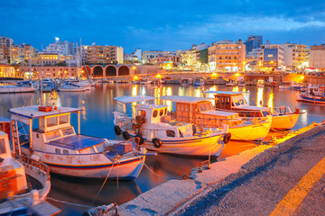 Old harbour of Heraklion with fishing boats and marina during twilight blue hour, Crete, Greece....