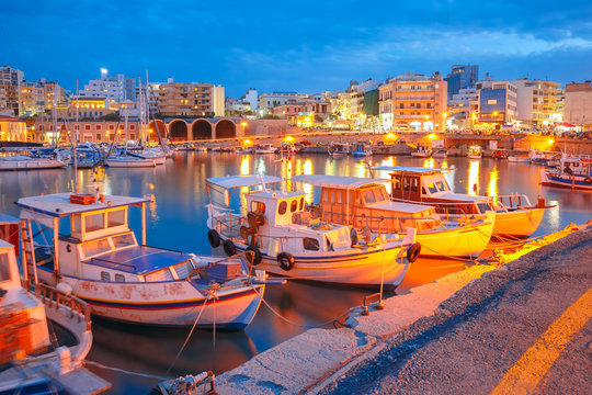 Fototapeta Old harbour of Heraklion with fishing boats and marina during twilight blue hour, Crete, Greece. Boats blurred motion on the foreground.