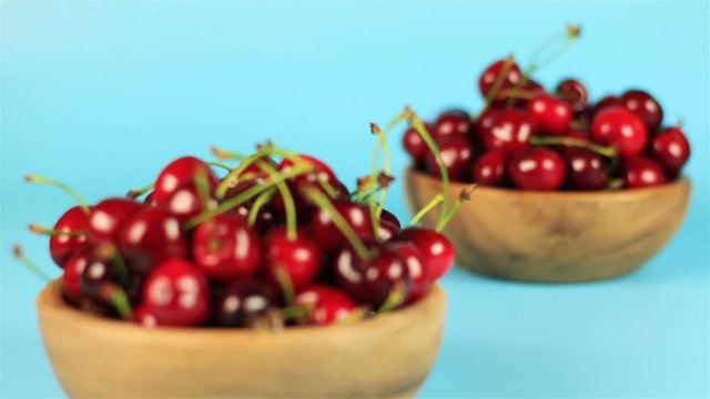 Two wooden bowls of cherries on blue background