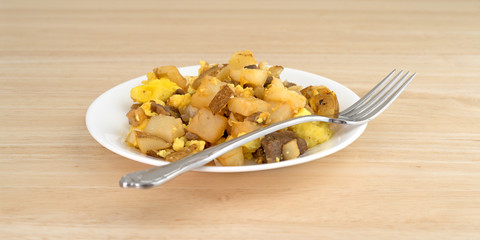 Breakfast meal with a fork on a plate atop a wood table top.