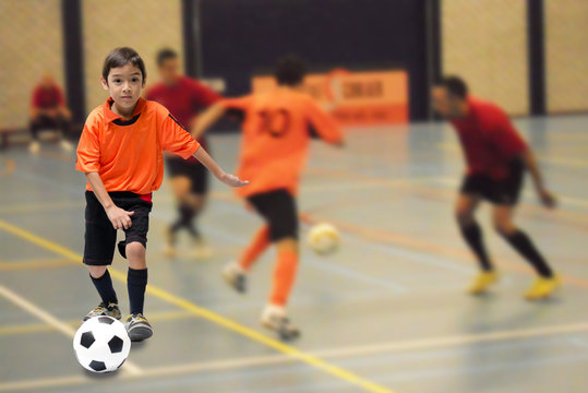 Little boy kicking football soccer ball indoor gym