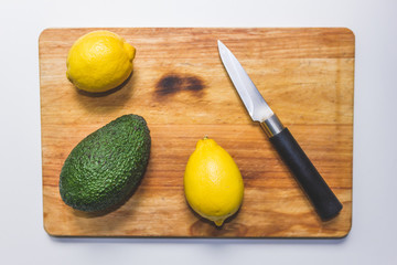 An avocado and two lemons on a chopping table.