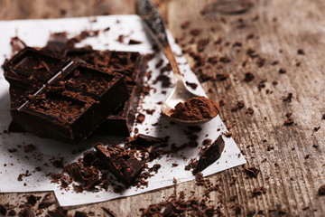 Spoon with cocoa powder and chocolate bar pieces  on wooden background