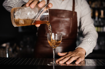 barman pouring alcoholic cocktail in glass