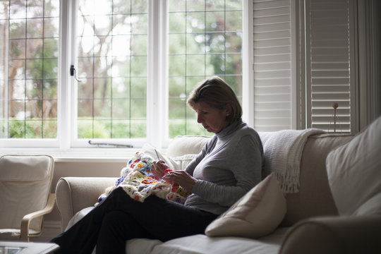 Close Up Of Woman Sitting On Sofa Making Crochet Blanket