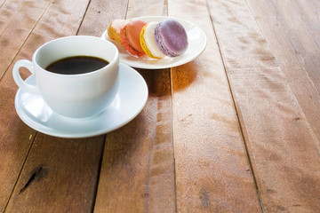 Black coffee in white cup with macaroon on old wood table.
