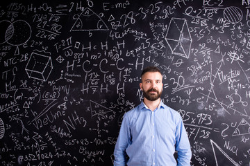 Hipster teacher against big blackboard with mathematical symbols