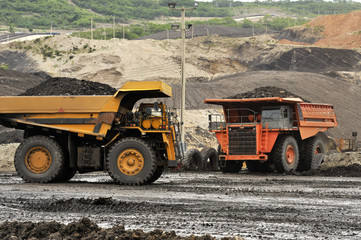 Yellow excavator loading soil on a truck at mine back lit