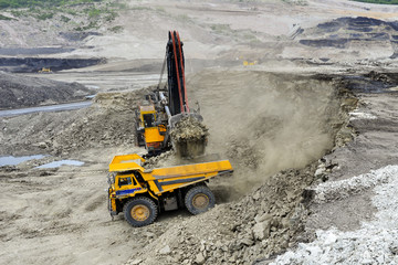 Yellow excavator loading soil on a truck at mine back lit